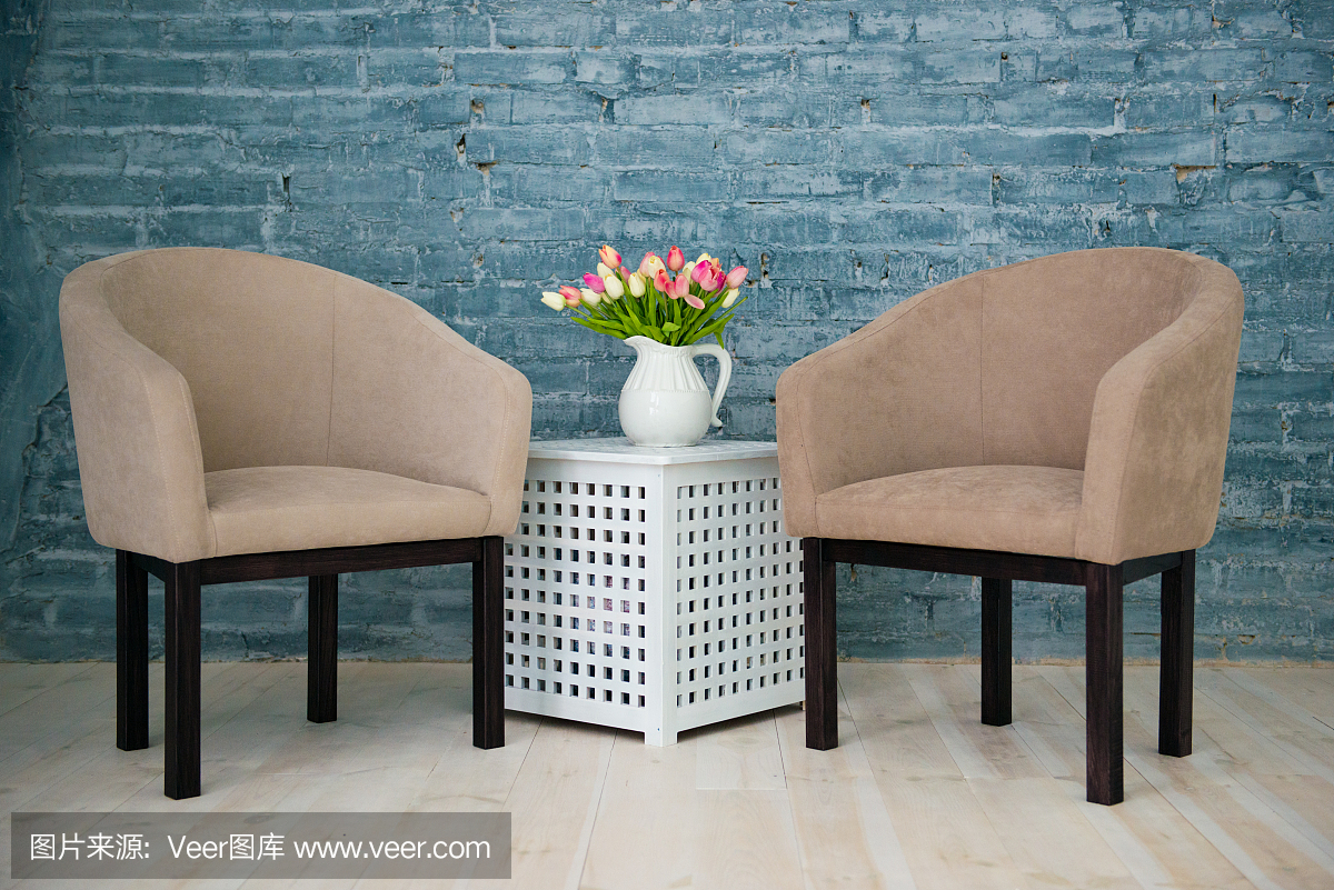 兩張灰色扶手椅、一張桌子和靠在灰色磚墻邊的花。室內(nèi)